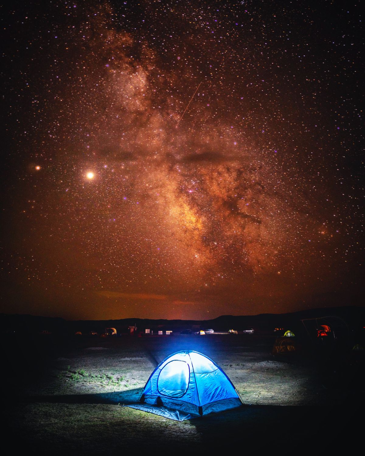 A glowing tent under a starry night sky
